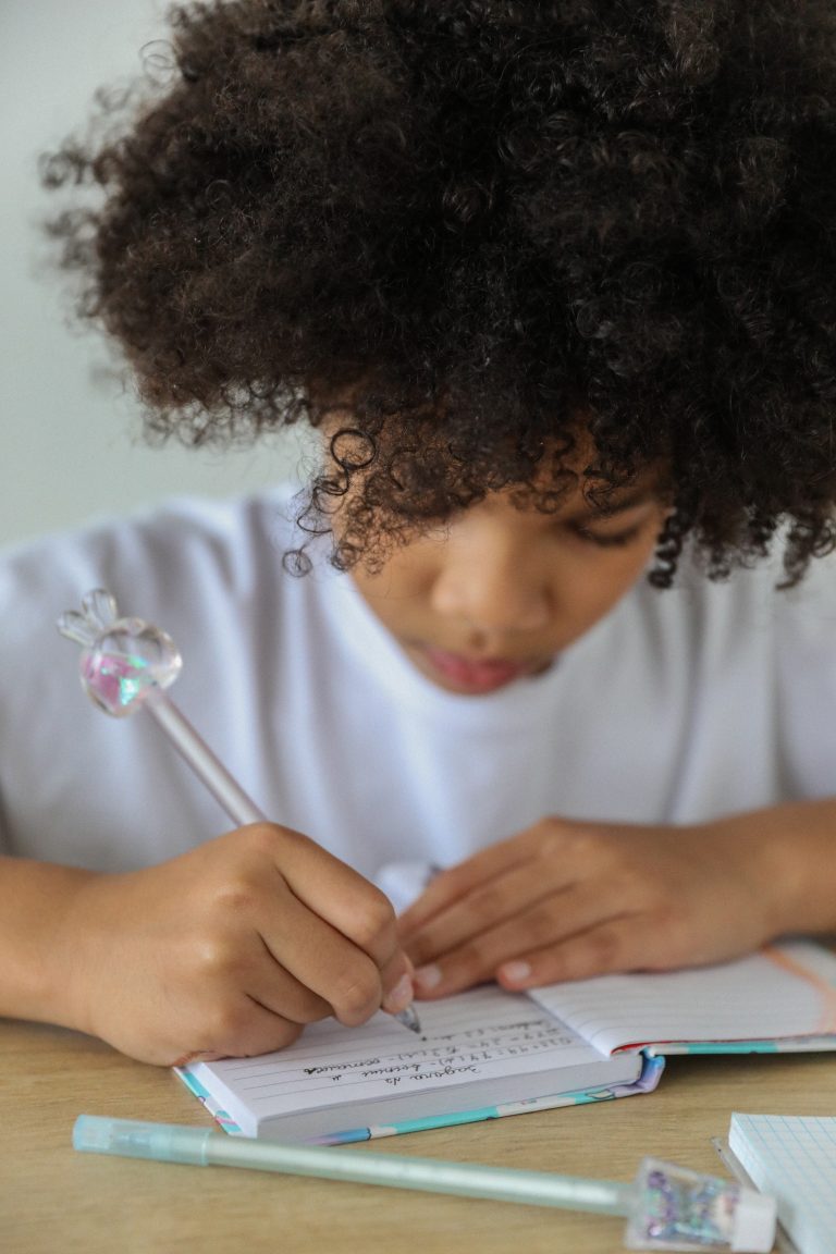 Crop African American schoolgirl writing in diary at desk