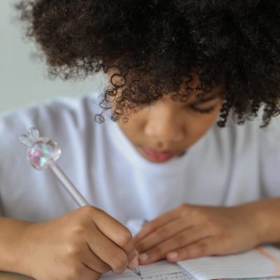 Crop African American schoolgirl writing in diary at desk