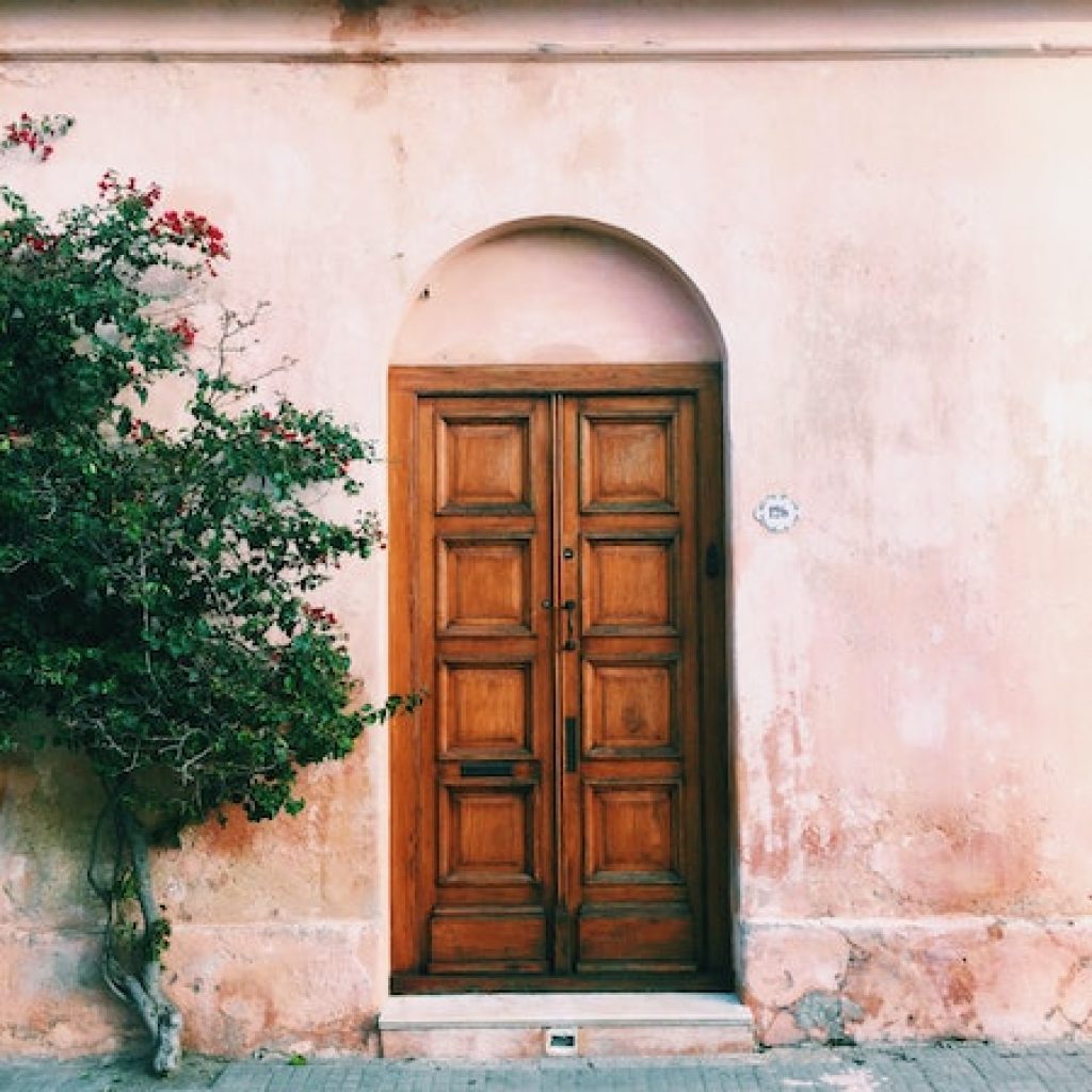Wooden front door along a blushed rose colored cement facade.