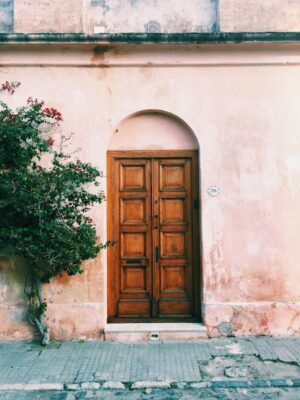 Wooden front door along a blushed rose colored cement facade.