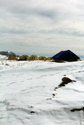 5 small brown tents next to a larger black tent in the snow