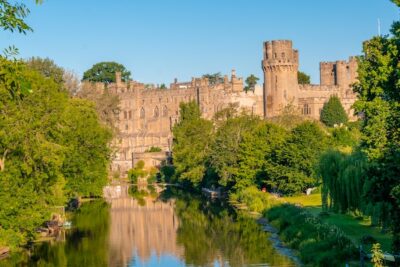 Medieval buildings in brown stone next to a small river with trees surrounding it on both sides