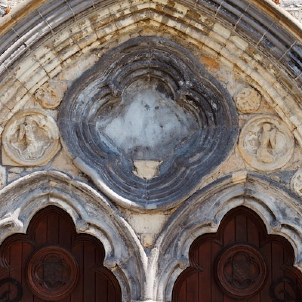 quatrefoil window outside of a church building hanging over two dark wooden doors