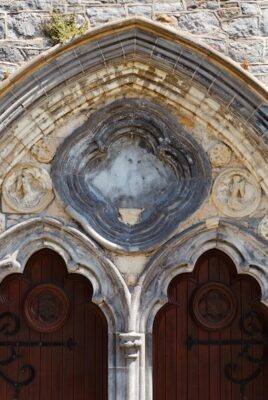 quatrefoil window outside of a church building hanging over two dark wooden doors